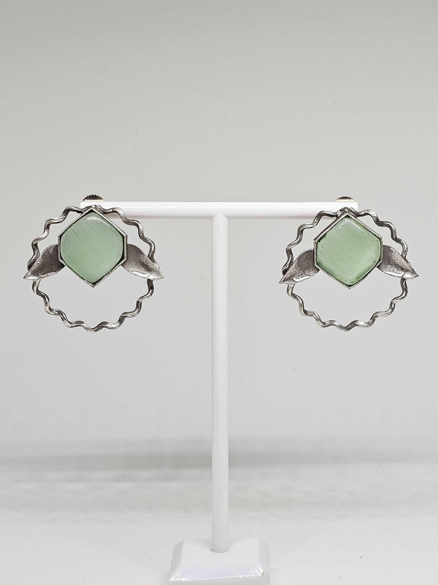 A pair of handcrafted lightweight brass stud earrings adorned with vibrant green Monalisa stones, designed in an elegant leaf shape, perfect for adding a touch of nature-inspired sophistication to any ensemble.