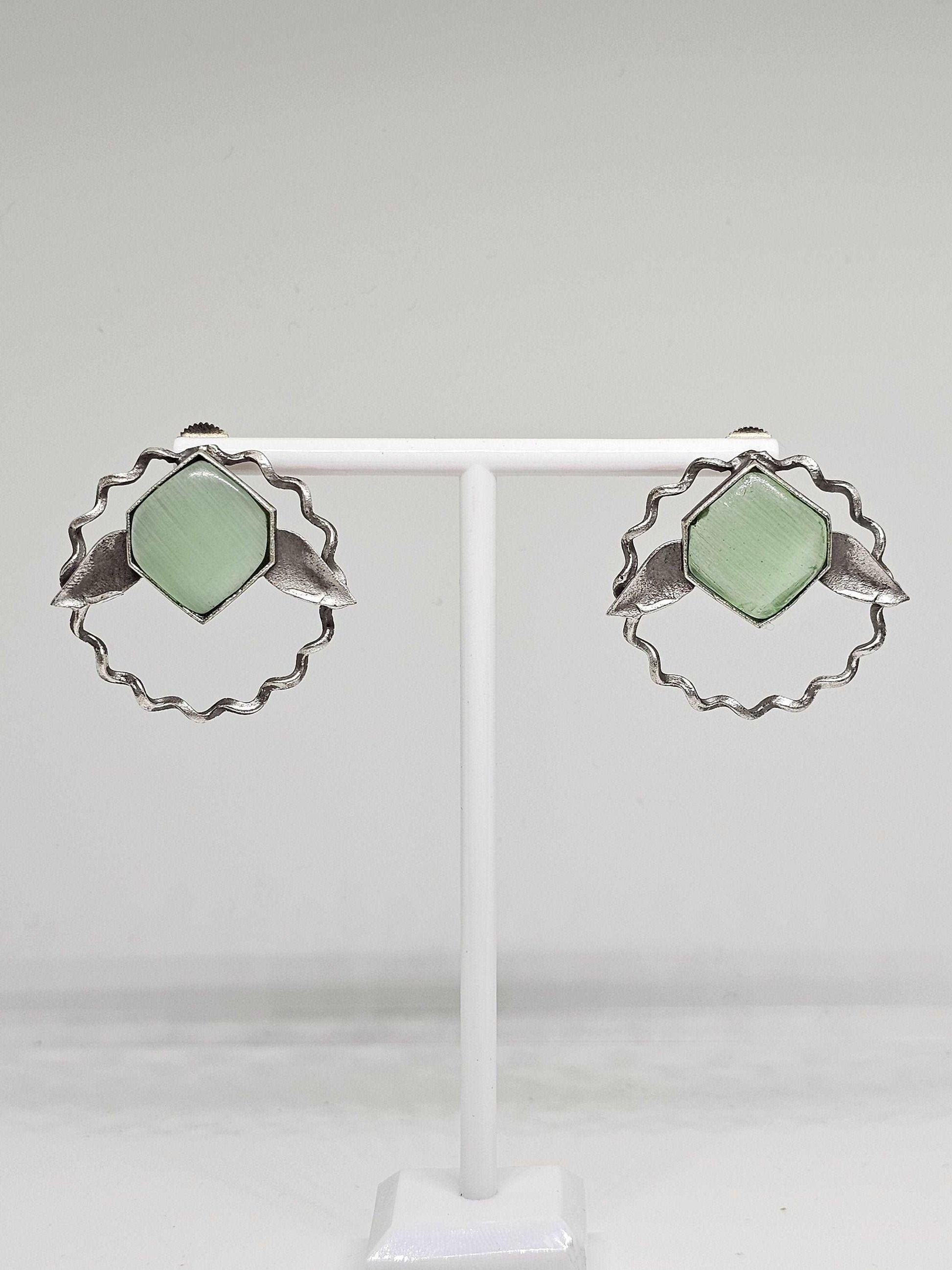 A pair of handcrafted lightweight brass stud earrings adorned with vibrant green Monalisa stones, designed in an elegant leaf shape, perfect for adding a touch of nature-inspired sophistication to any ensemble.