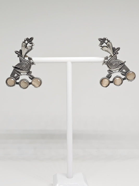 Exquisite handcrafted oxidized silver bird earrings featuring an intricate leaf design with delicate gemstone accents, beautifully displayed on a white stand.