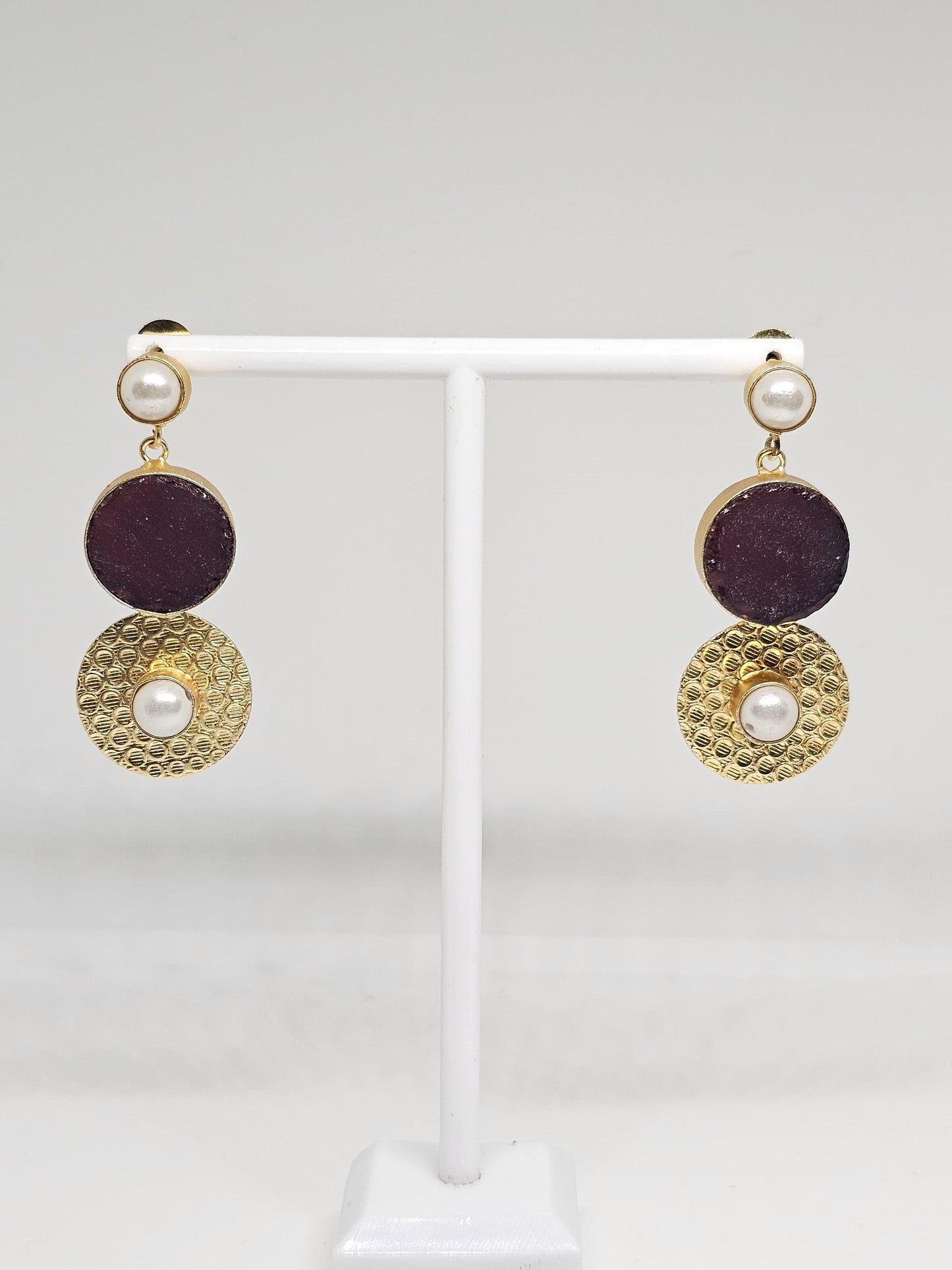 Elegant gold-plated earrings with purple stone and pearl accents shown in close-up on a display stand