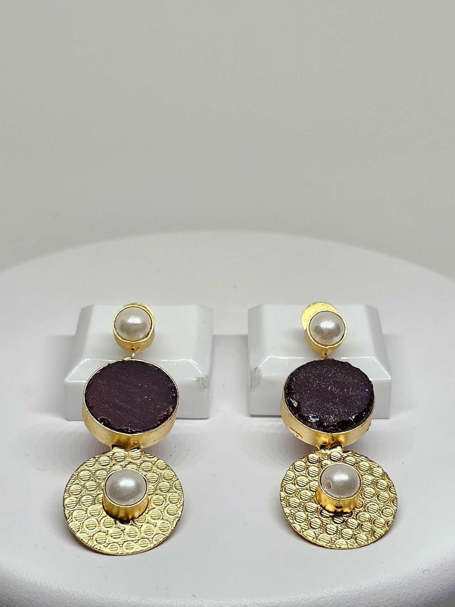 Handmade gold-plated double drop earrings featuring a purple stone and pearl accents displayed on a white stand