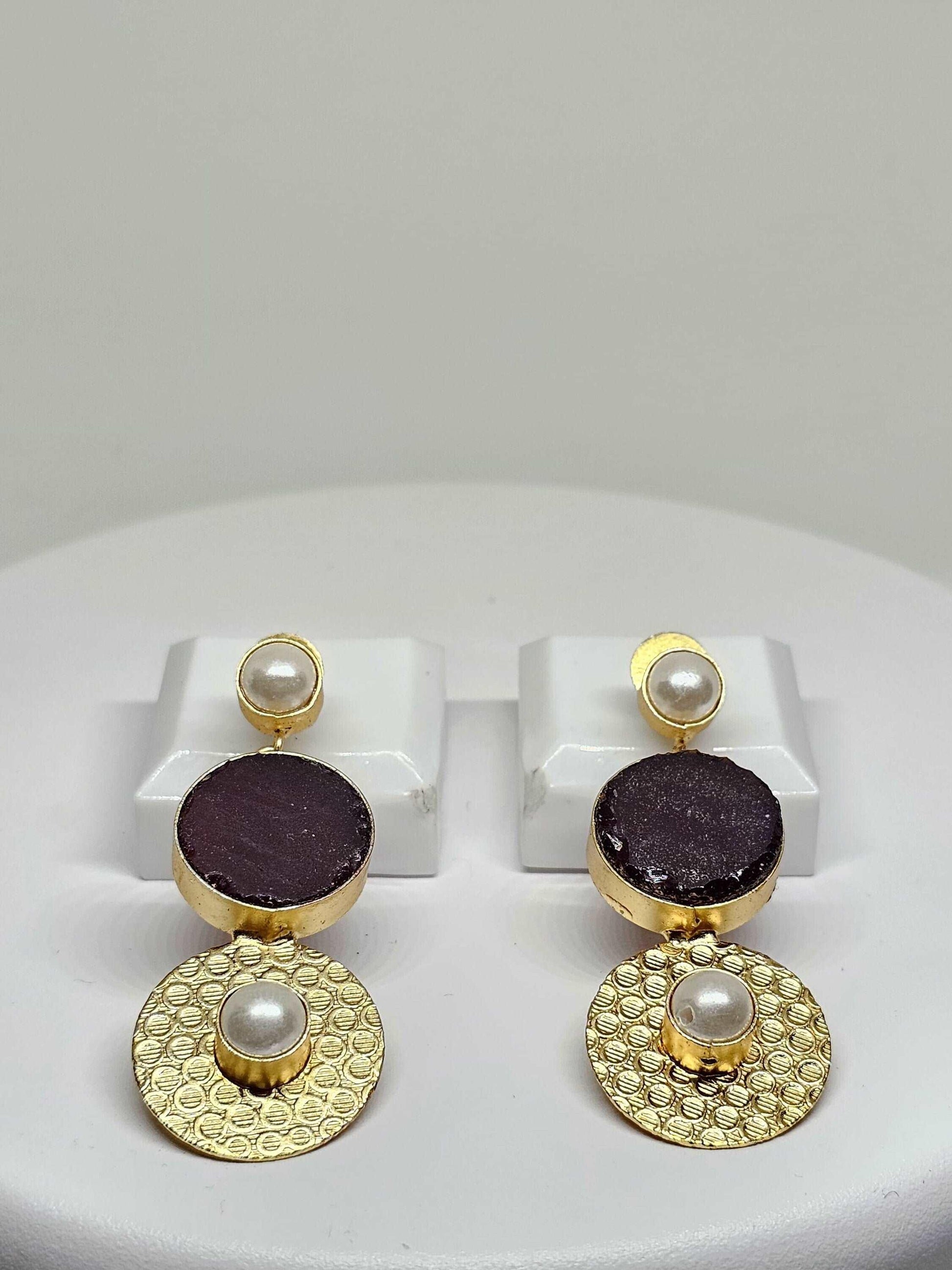 Handmade gold-plated double drop earrings featuring a purple stone and pearl accents displayed on a white stand