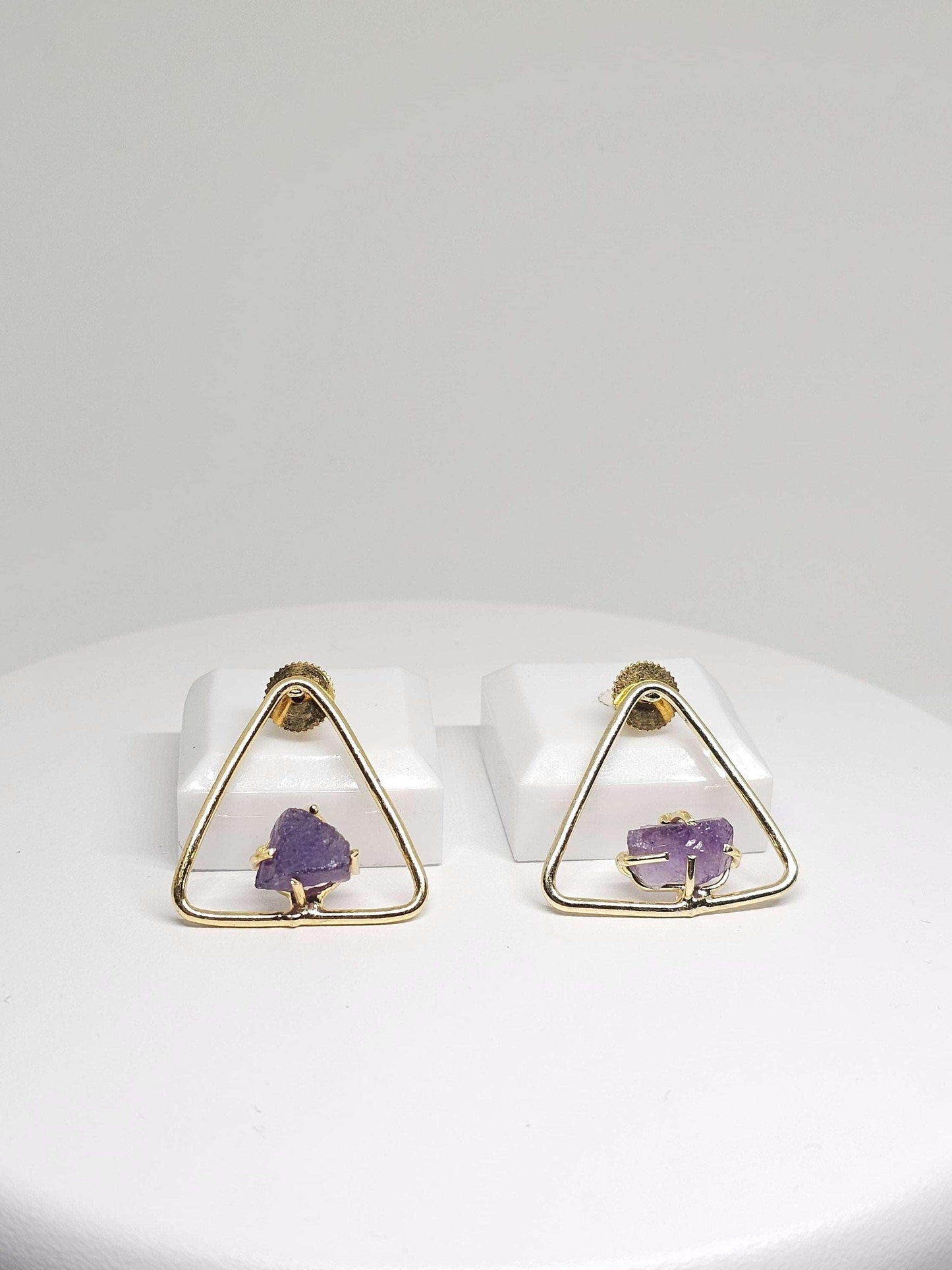 Stylish triangle brass earrings with raw amethyst gemstones, displaying a contemporary geometric shape and natural amethyst textures.