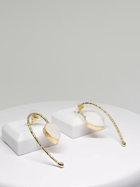 Handcrafted brass and white stone curved dangle earrings displayed on white stands, showcasing elegant minimalist design