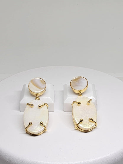 Gold-plated dangle earrings with oval-shaped Mother of Pearl stones on a white display stand
