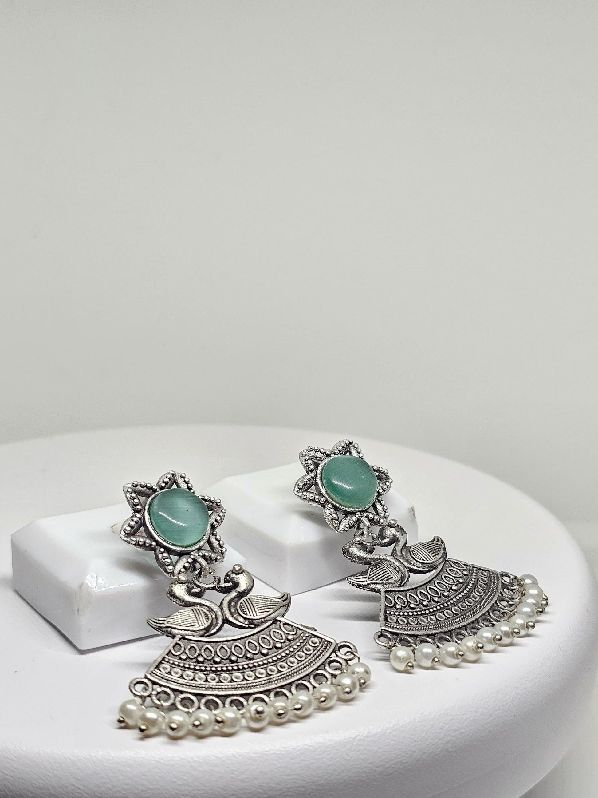 Traditional oxidized silver earrings with intricate duck designs, green stone, and pearl accents