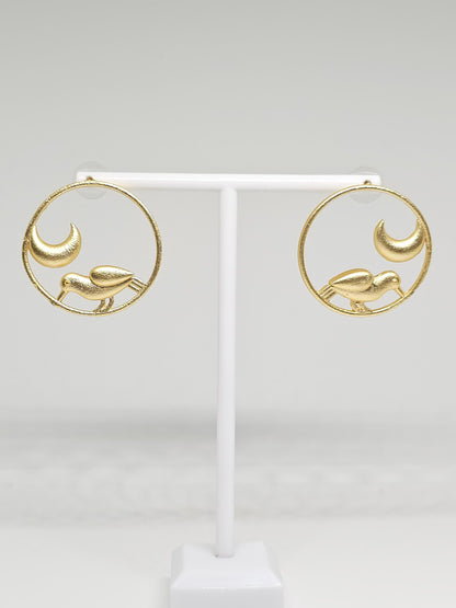 Brass hoop earrings with bird and crescent moon design on display stand.
