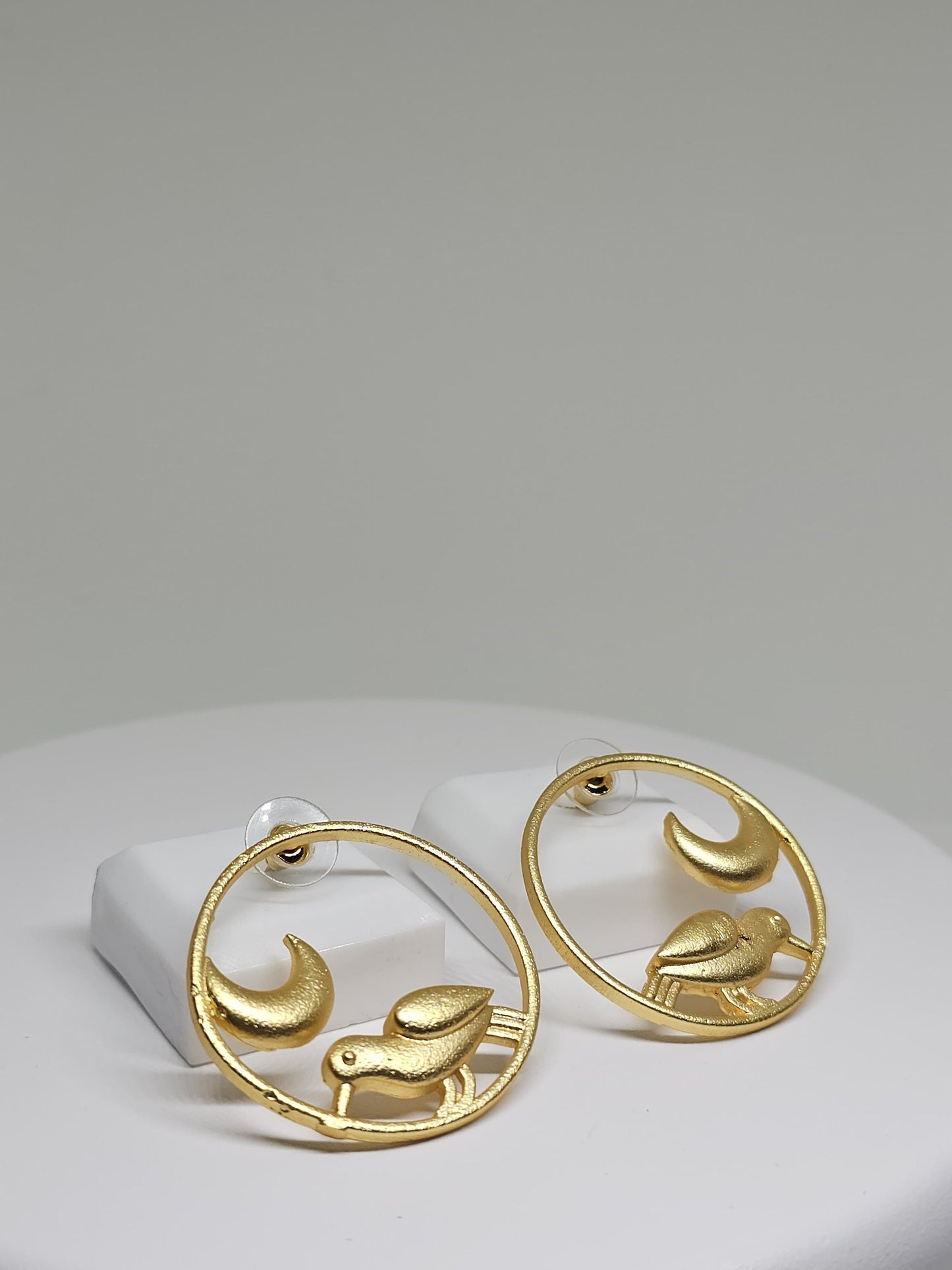 Close-up of gold-tone brass earrings featuring bird and moon motif