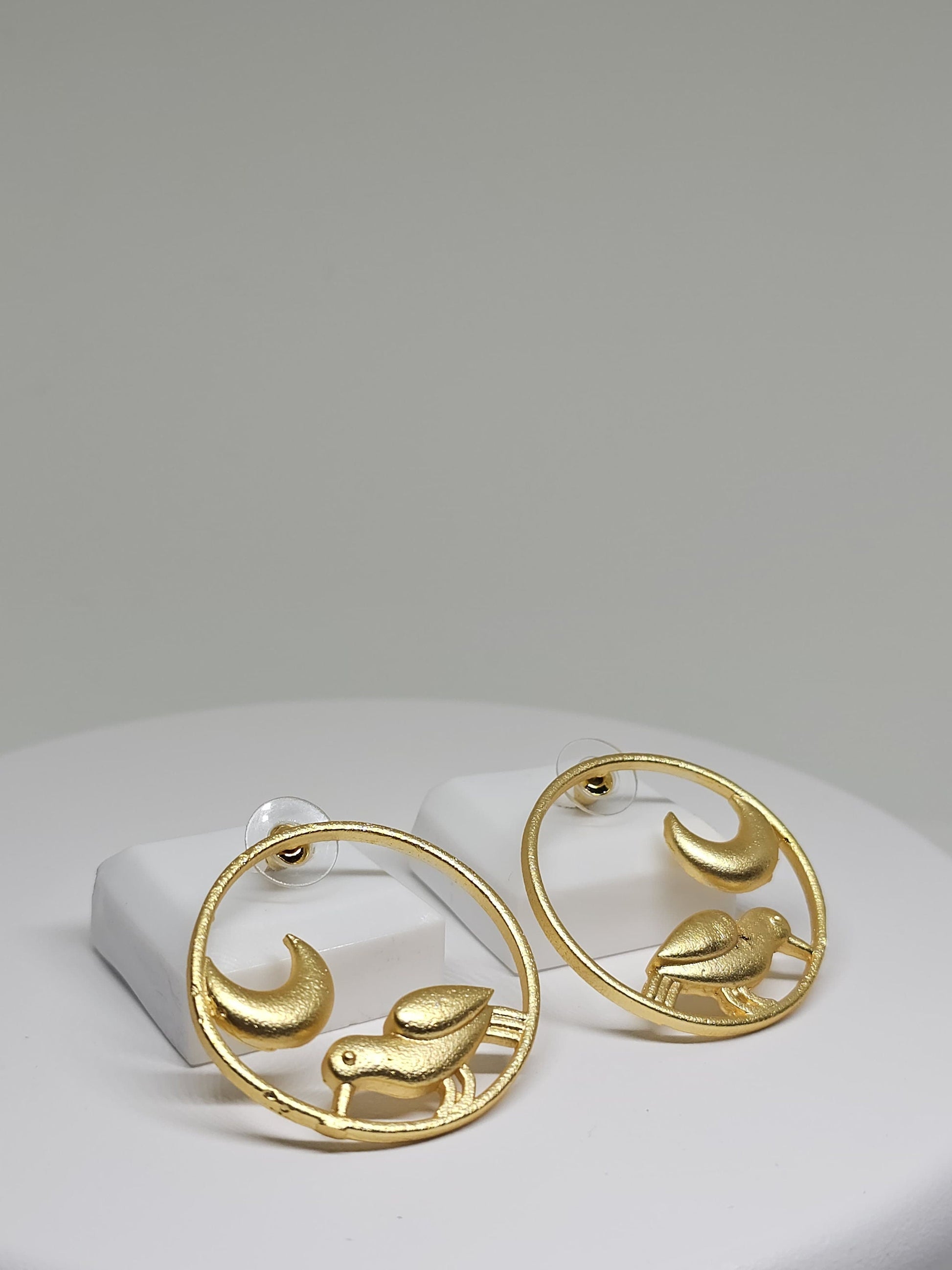 Close-up of gold-tone brass earrings featuring bird and moon motif