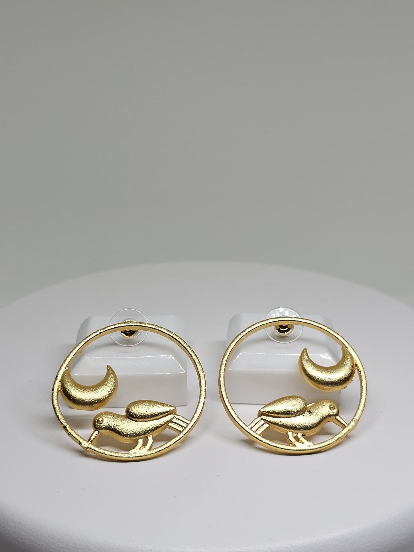Side view of minimalist bird and crescent moon brass hoop earrings