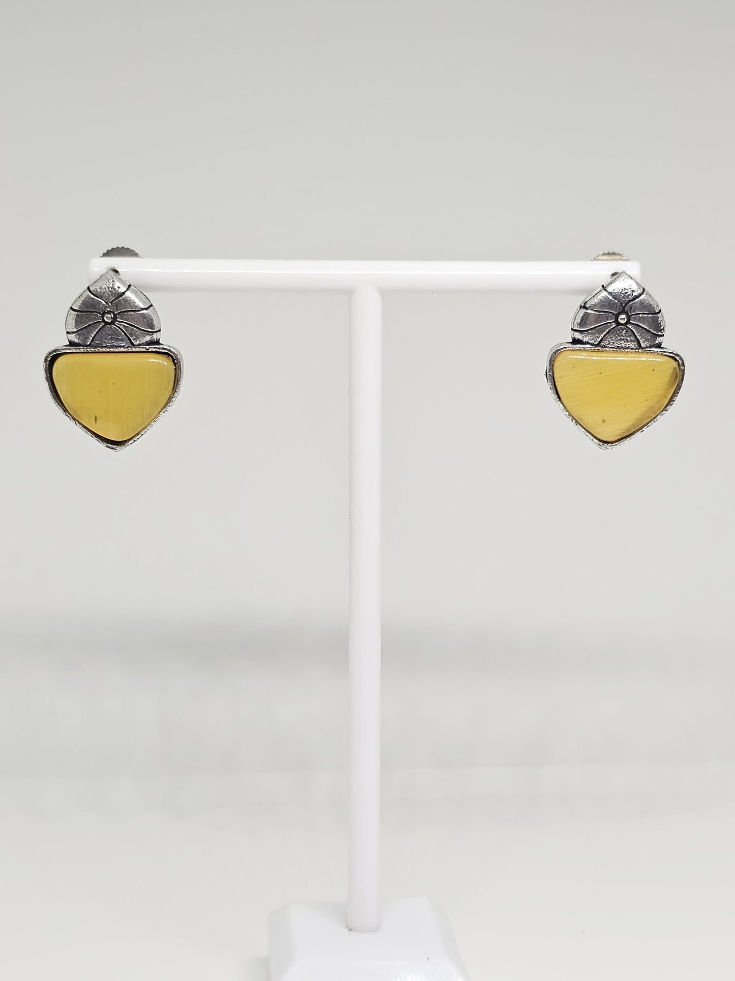 Close-up of silver-tone stud earrings with floral design and Yellow stone accent.