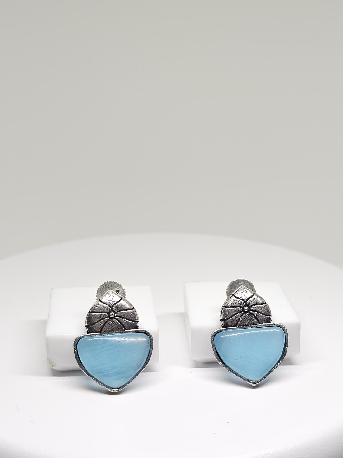 Silver floral stud earrings with blue stone on a white display stand