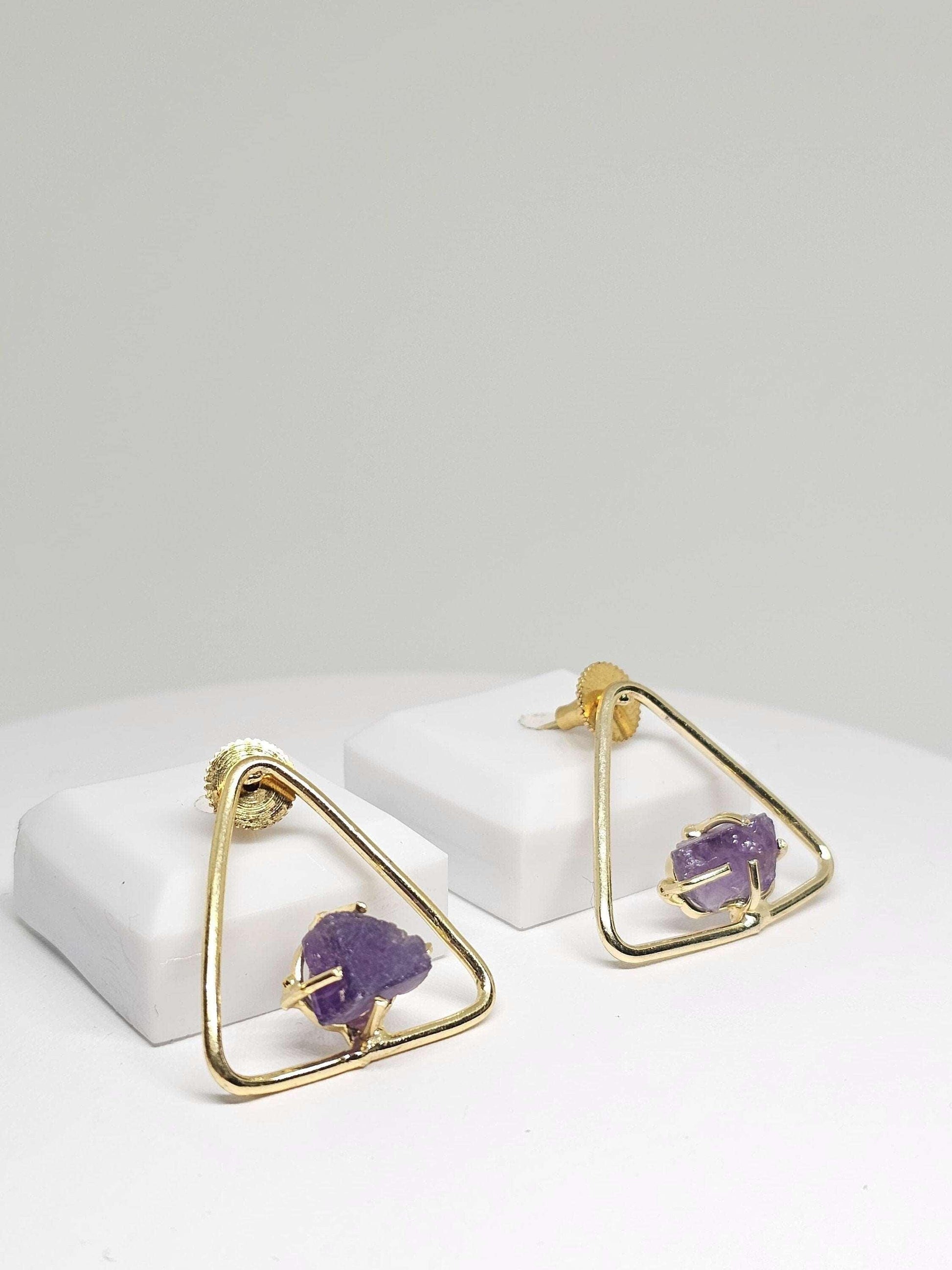 Close-up of elegant triangle brass earrings adorned with raw amethyst stones, highlighting the modern geometric design and natural purple hues