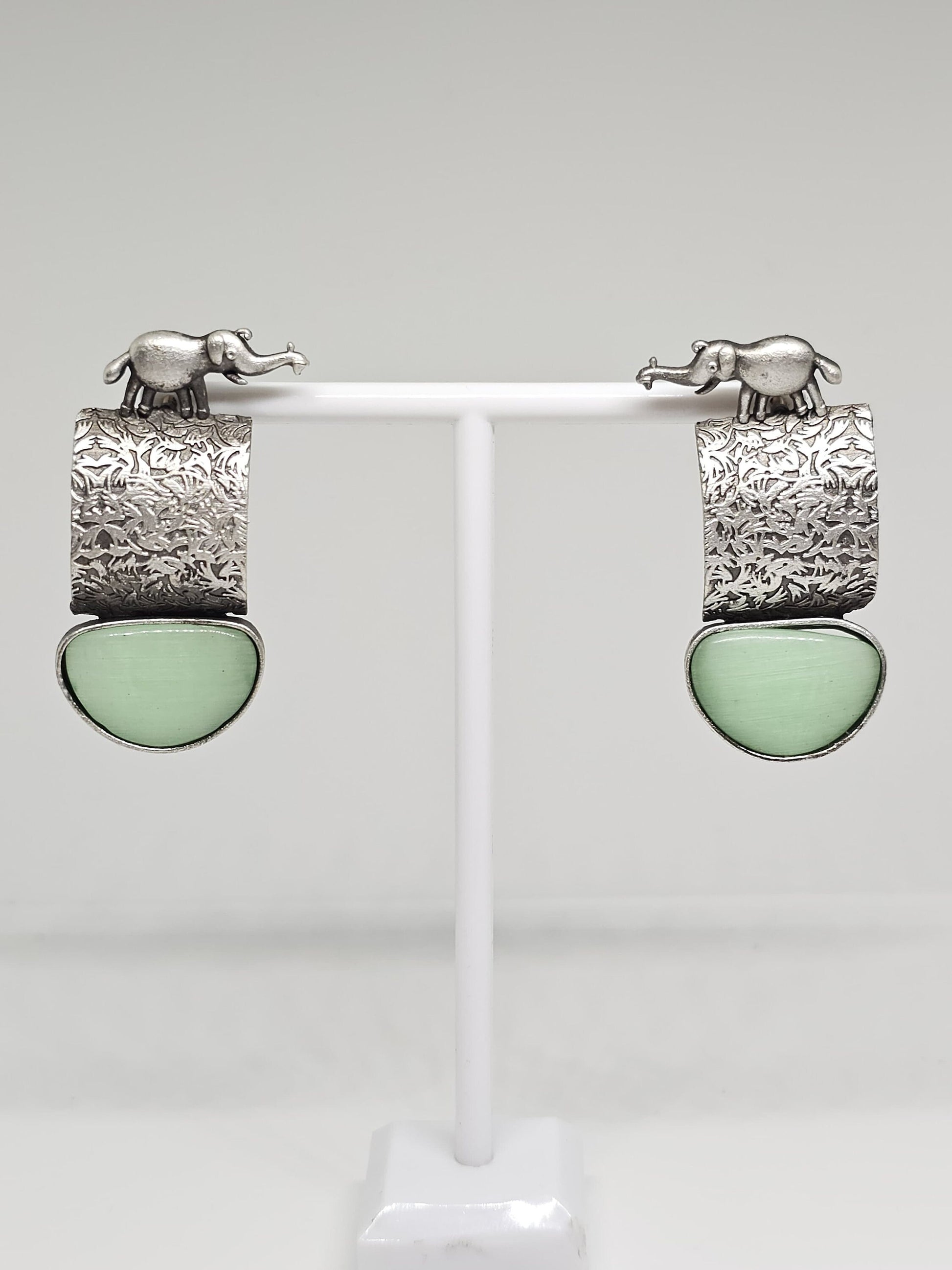 Silver-plated earrings with green stone and elephant design on display.