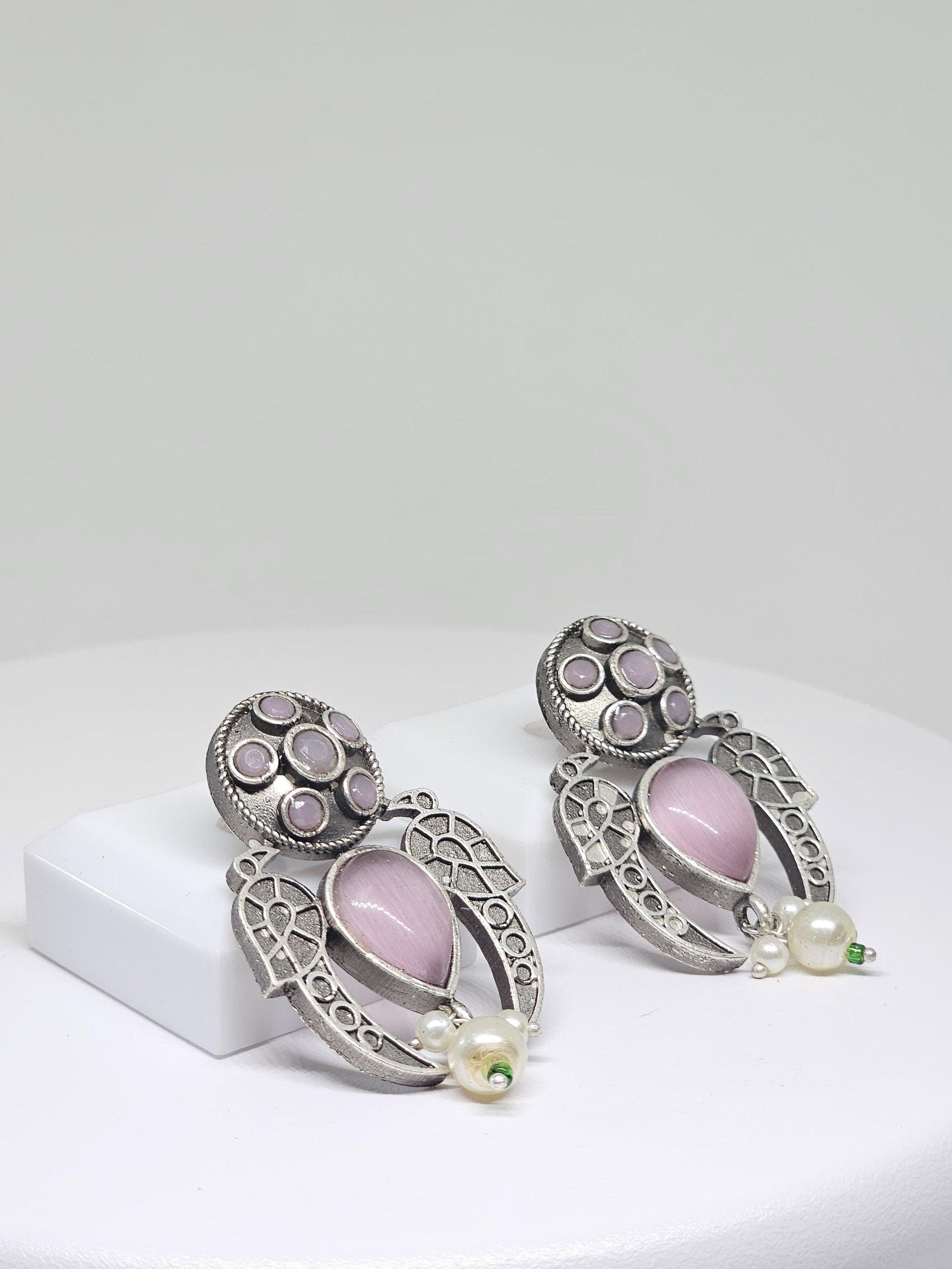 Close-up of vintage silver tribal earrings with pink teardrop stones and pearl accents
