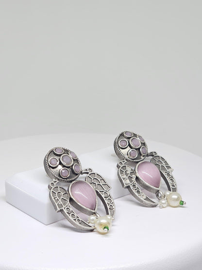 Close-up of vintage silver tribal earrings with pink teardrop stones and pearl accents