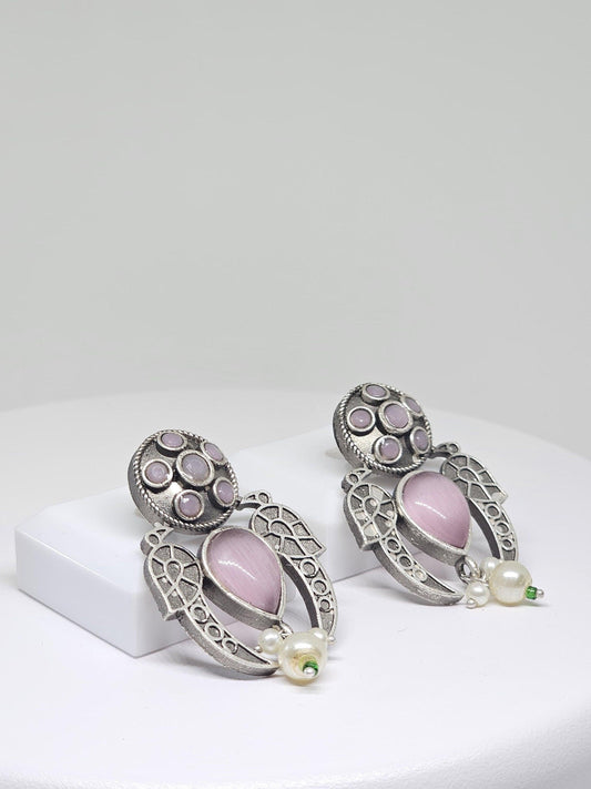 Close-up of vintage silver tribal earrings with pink teardrop stones and pearl accents