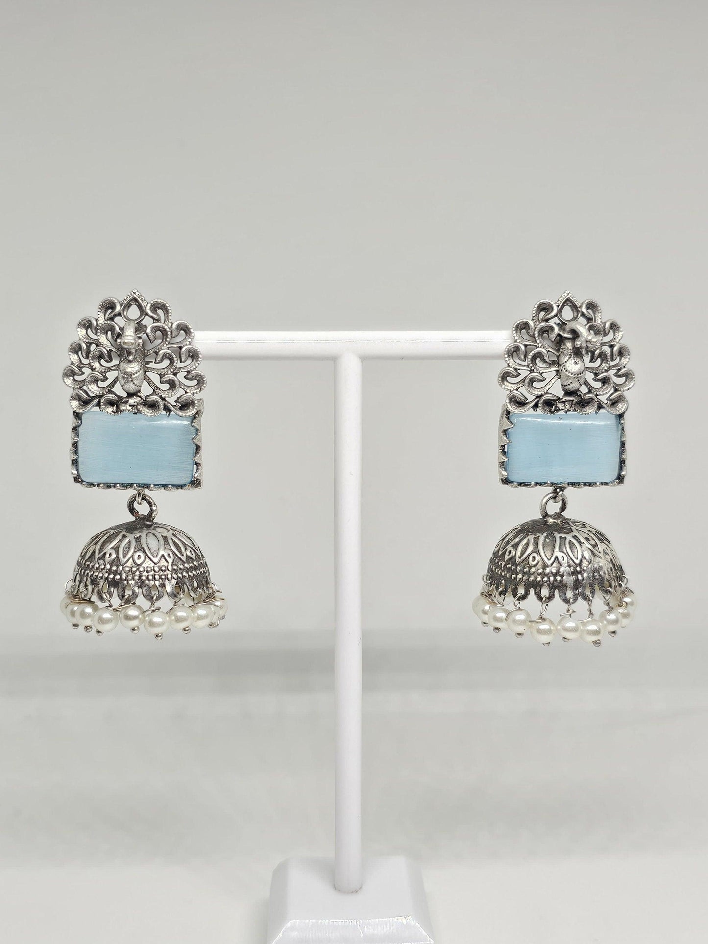 Silver jhumka earrings with blue stone and pearl dangles on display stand