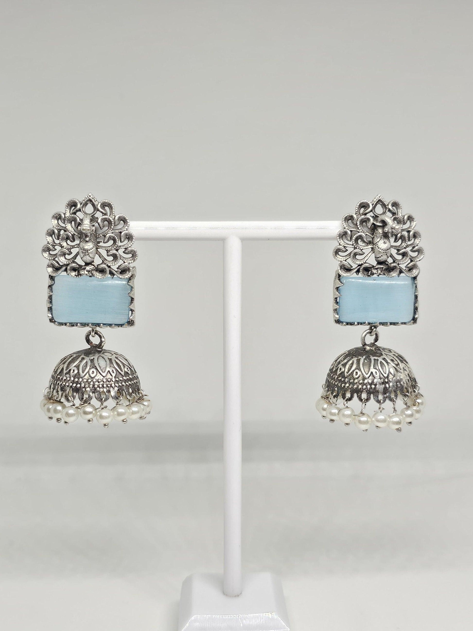 Silver jhumka earrings with blue stone and pearl dangles on display stand