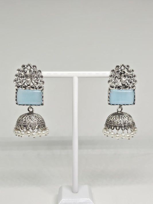 Silver jhumka earrings with blue stone and pearl dangles on display stand