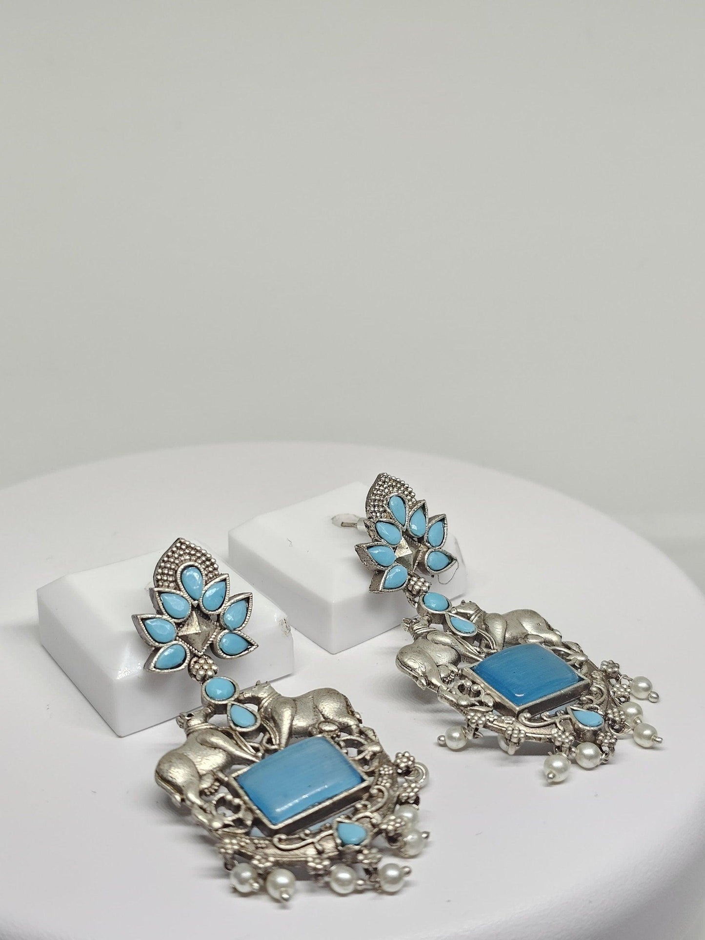 Handmade ethnic earrings featuring bull motifs, blue stones, and pearl details in oxidized silver