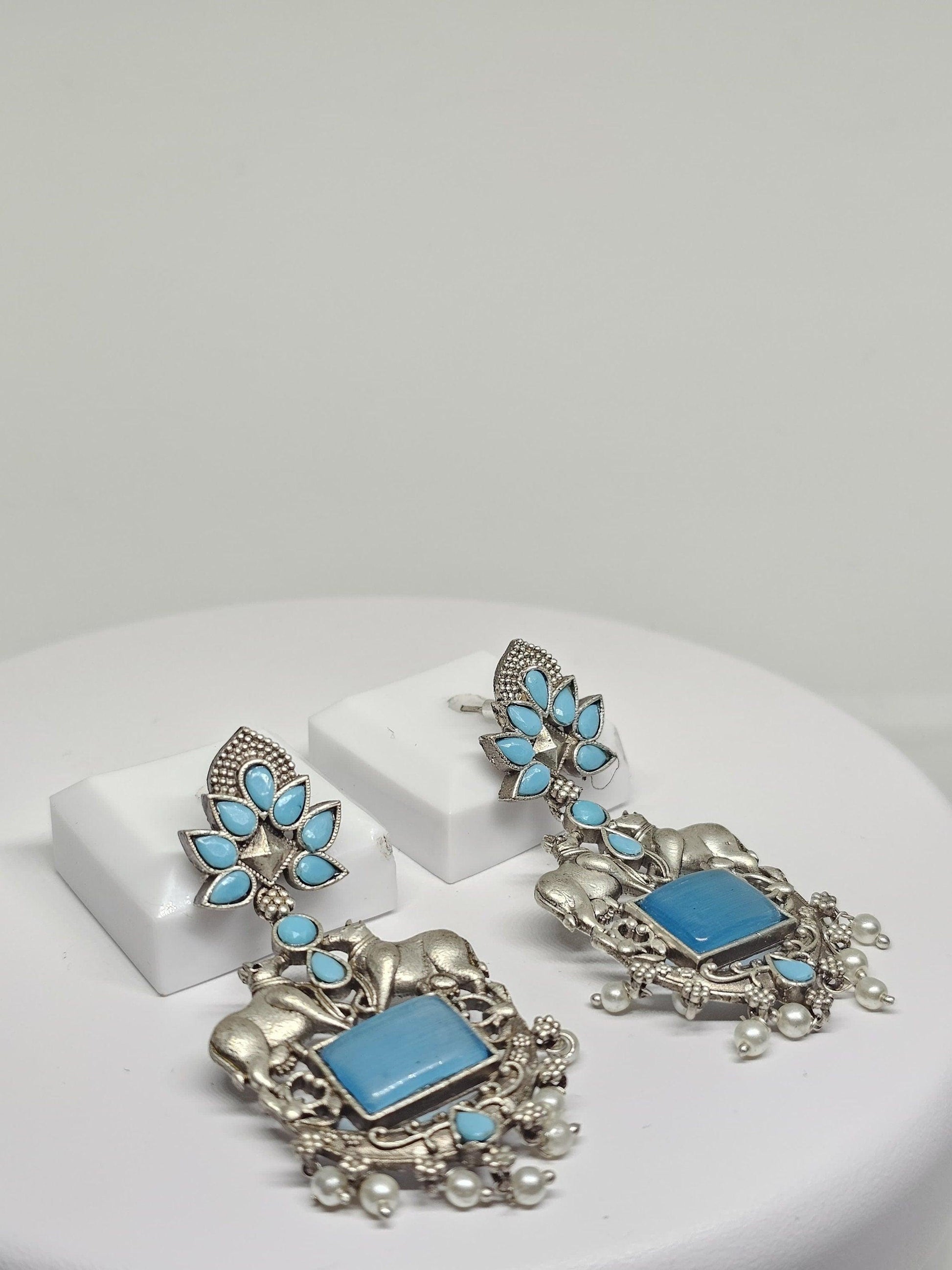 Handmade ethnic earrings featuring bull motifs, blue stones, and pearl details in oxidized silver