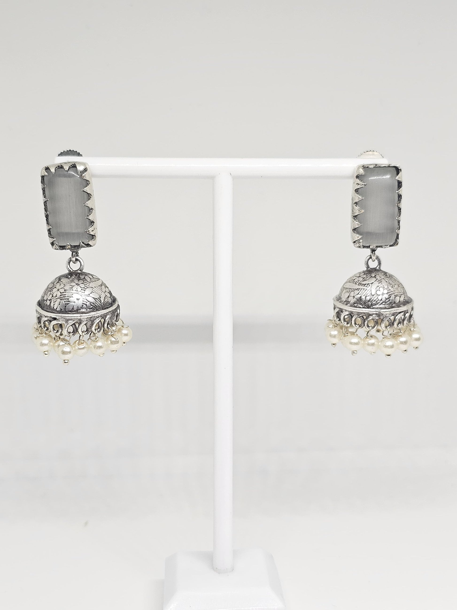 Silver jhumka earrings with grey stone and pearl dangles on display stand