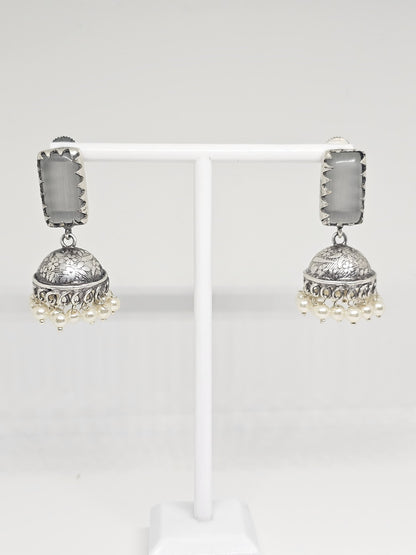 Silver jhumka earrings with grey stone and pearl dangles on display stand