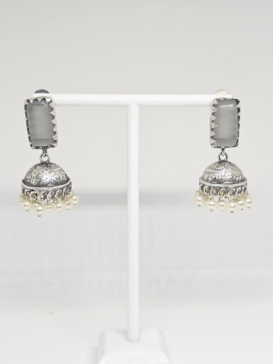 Silver jhumka earrings with grey stone and pearl dangles on display stand