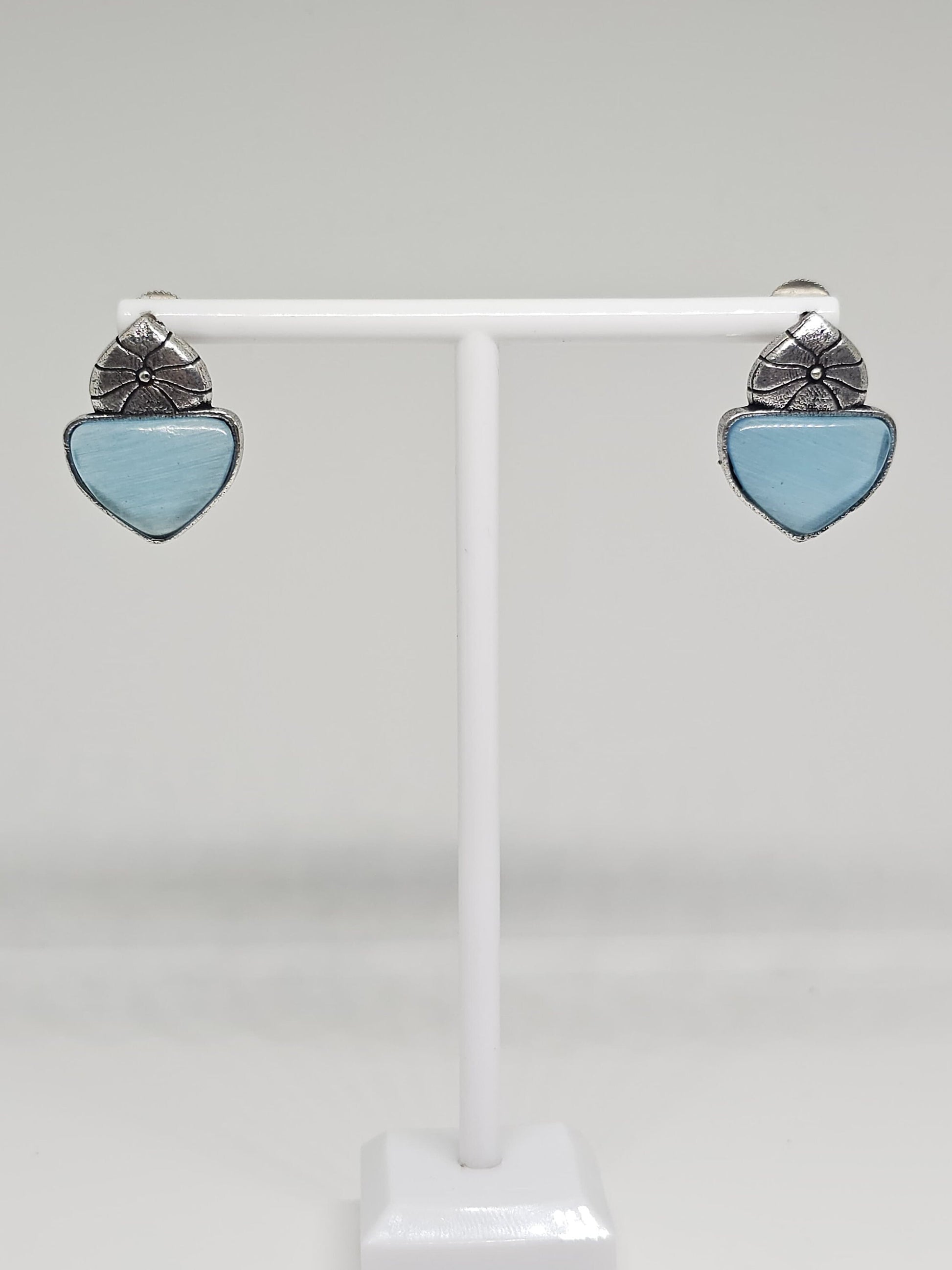 Close-up of silver-tone stud earrings with floral design and blue stone accent.