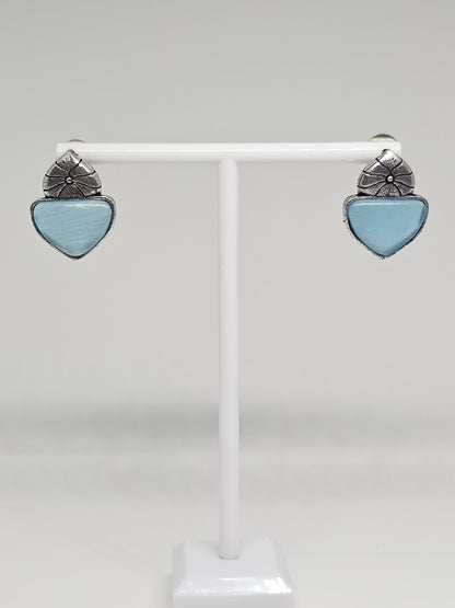 Close-up of silver-tone stud earrings with floral design and blue stone accent.