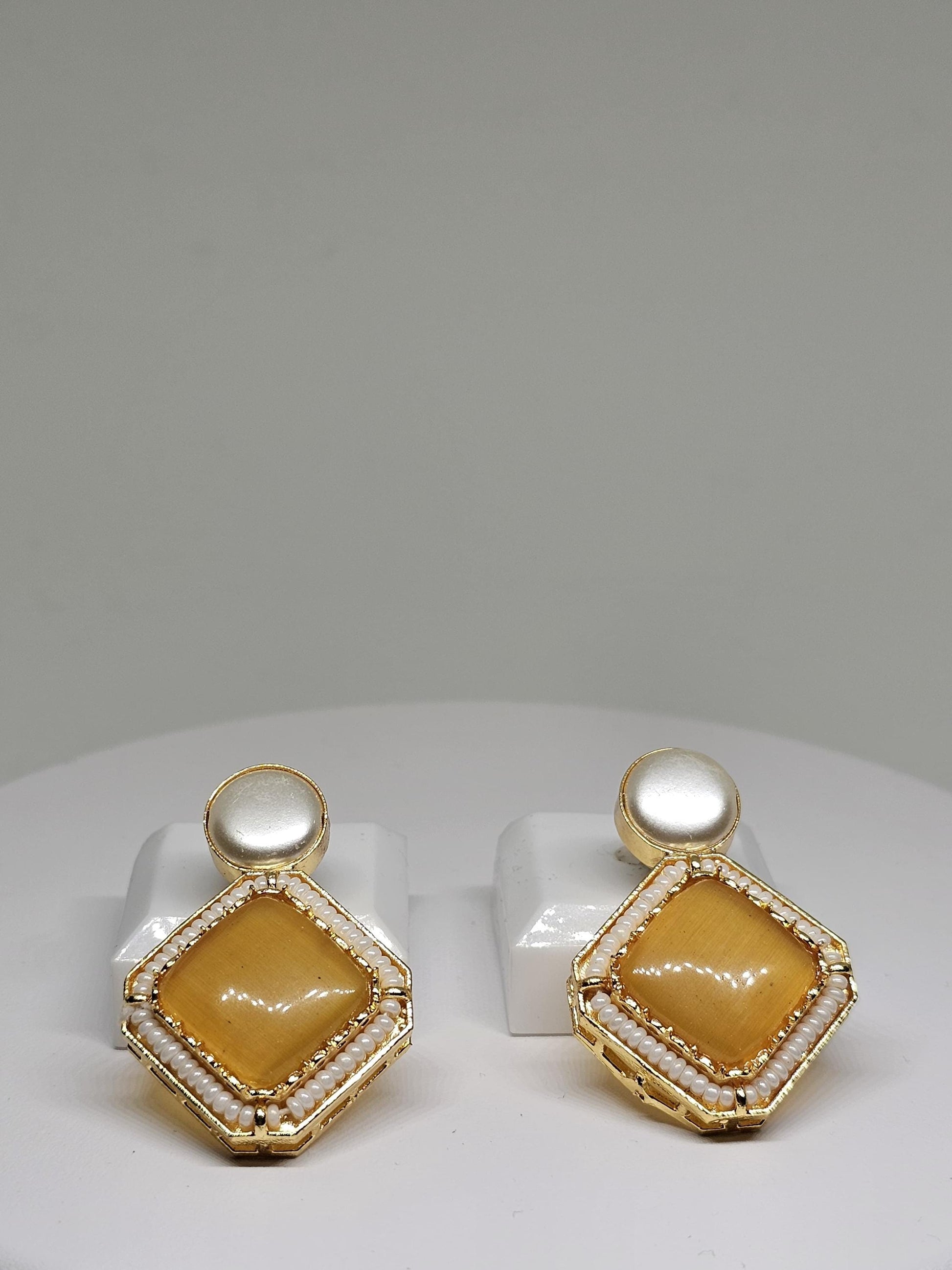 Luxury gold-tone earrings with a vibrant yellow stone, highlighted by a delicate bead frame and topped with a luminous pearl for timeless elegance